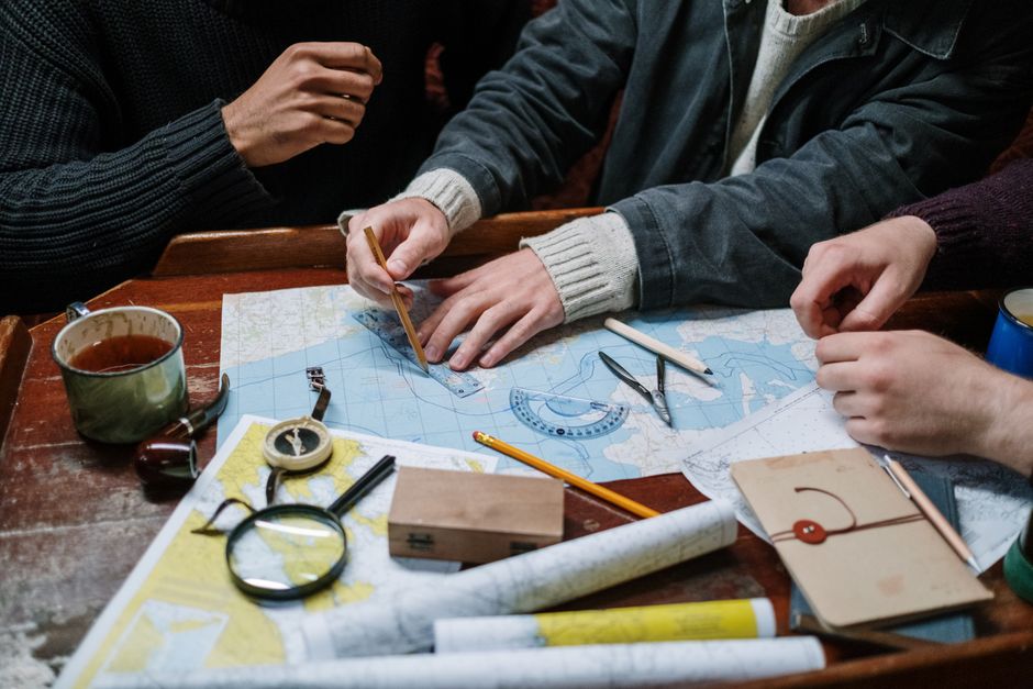 Adults planning a nautical journey using maps, compass, and tools indoors.